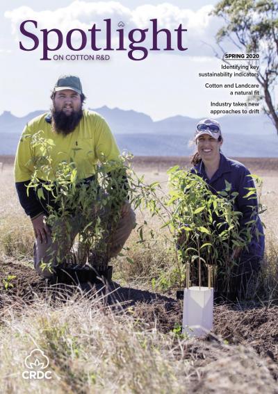 Two researchers kneeling in a paddock behind trees they have just planted for biodiversity. 